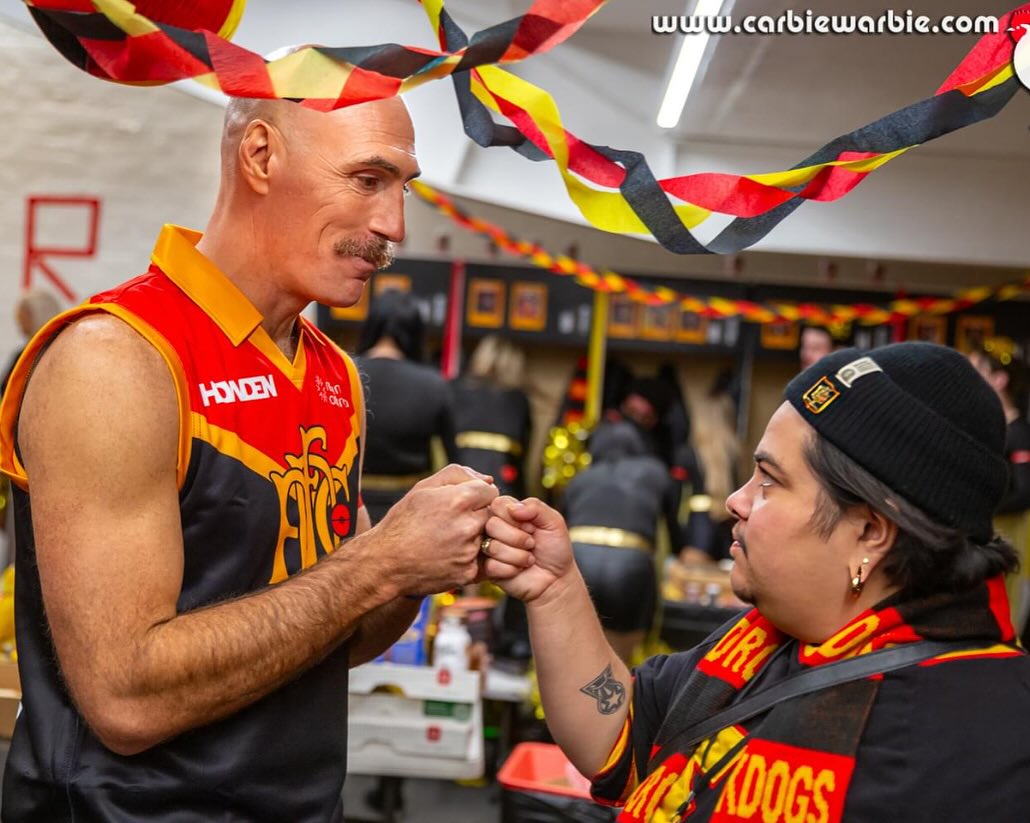 Brian in the red, black and gold Rockdogs guernsey, fist-bumping a teammate in the streamer-draped changerooms before the match